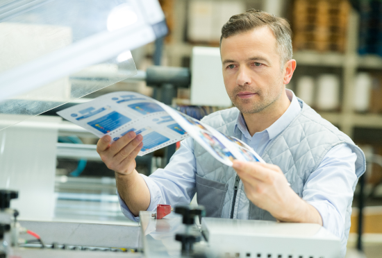 A male warehouse printer technician reviewing quality print collateral